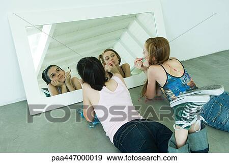 Two young friends lying on the ground, holding lipstick, one looking at self in mirror View Large Photo Image Stock Photo - Two young friends lying on the ground, holding lipstick, one looking at self in mirror. Fotosearch