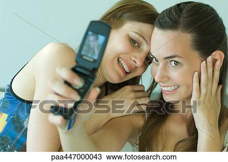 Two young friends photographing selves with cell phone, smiling View Large Photo Image Stock Image - Two young friends photographing selves with cell phone, smiling. Fotosearch