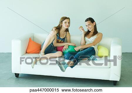 Two young friends sitting on couch, smiling at camera, full length View Large Photo Image Stock Photography - Two young friends sitting on couch, smiling at camera, full length. Fotosearch