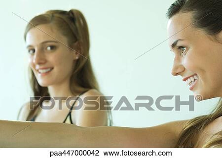Two young friends smiling, one looking at camera, side view View Large Photo Image Stock Image - Two young friends smiling, one looking at camera, side view. Fotosearch