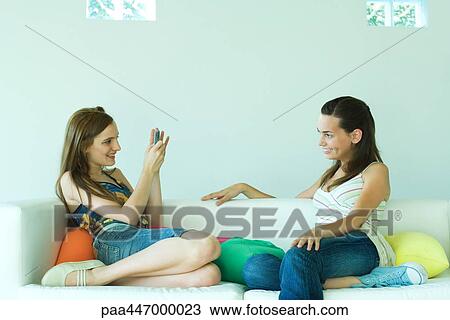 Young woman on couch photographing friend with cell phone View Large Photo Image Stock Image - Young woman on couch photographing friend with cell phone. Fotosearch