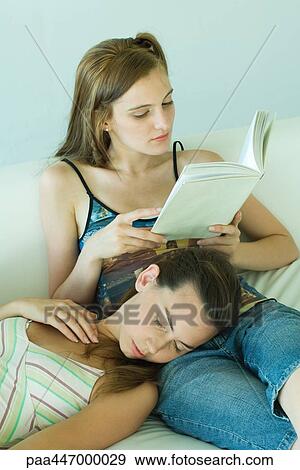 Young woman on couch reading book, friend resting head on her lap with eyes closed View Large Photo Image Stock Photo - Young woman on couch reading book, friend resting head on her lap with eyes closed. Fotosearch