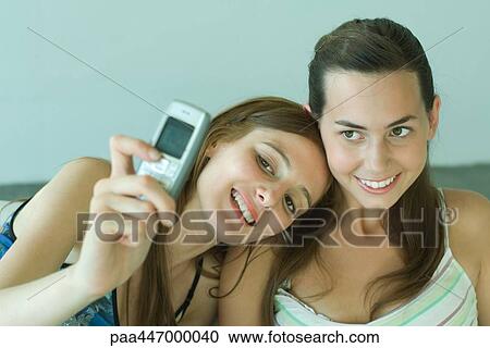 Young woman photographing self with friend, holding up cell phone View Large Photo Image Stock Image - Young woman photographing self with friend, holding up cell phone. Fotosearch