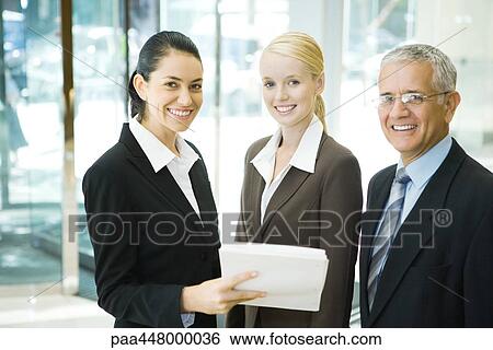Business associates smiling at camera, one woman holding stack of documents View Large Photo Image Stock Photograph - Business associates smiling at camera, one woman holding stack of documents. Fotosearch
