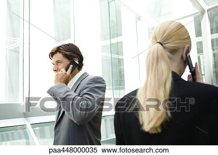 Stock Photography - Business associates walking past each other in hallway, using cell phones. Fotosearch