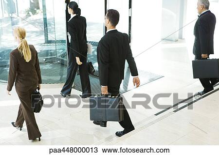 Stock Image - Business associates with briefcases exiting office lobby. Fotosearch