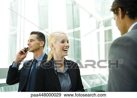 Business colleagues in hallway, woman laughing, man in background using cell phone View Large Photo Image Stock Photo - Business colleagues in hallway, woman laughing, man in background using cell phone. Fotosearch