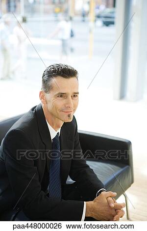 Stock Photograph - Businessman sitting in office lobby with hands clasped. Fotosearch
