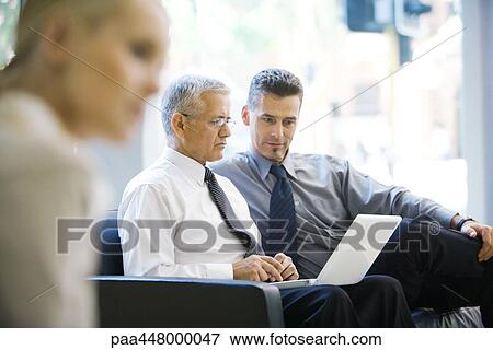 Two business associates looking at laptop together in lobby View Large Photo Image Stock Photo - Two business associates looking at laptop together in lobby. Fotosearch