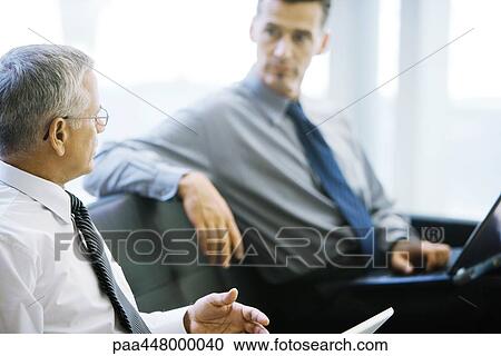 Two male business associates, sitting on sofa, talking View Large Photo Image Stock Image - Two male business associates, sitting on sofa, talking. Fotosearch