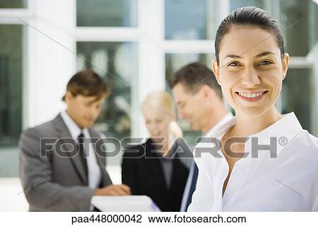Young businesswoman smiling, associates talking about contract in background View Large Photo Image Stock Image - Young businesswoman smiling, associates talking about contract in background. Fotosearch