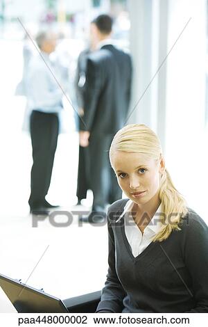 Young businesswoman using laptop, looking at camera, associates in background View Large Photo Image Stock Image - Young businesswoman using laptop, looking at camera, associates in background. Fotosearch