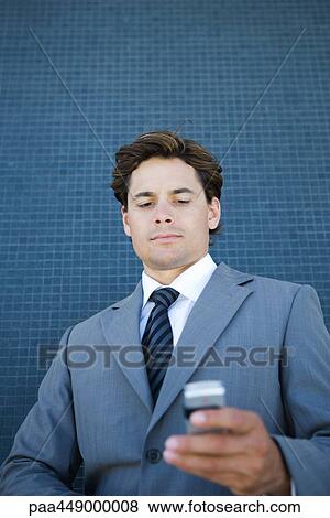Stock Photo - Businessman looking down at cell phone, low angle view. Fotosearch