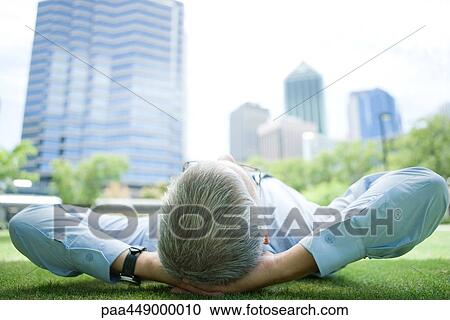 Businessman lying on grass, hands behind head View Large Photo Image Stock Image - Businessman lying on grass, hands behind head. Fotosearch