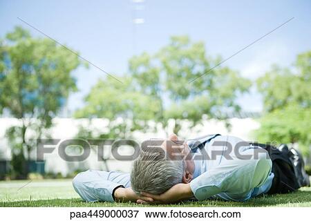 Stock Photo - Businessman lying on grass, hands behind head. Fotosearch