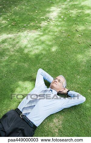 Stock Image - Businessman lying on grass with hands behind head. Fotosearch