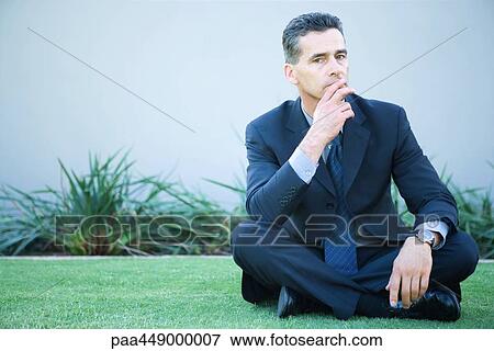 Businessman sitting cross-legged on grass, fingers over lips View Large Photo Image Stock Photo - Businessman sitting cross-legged on grass, fingers over lips. Fotosearch