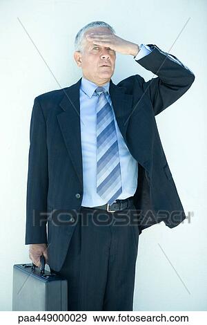 Businessman standing, holding briefcase, hand over forehead View Large Photo Image Stock Photo - Businessman standing, holding briefcase, hand over forehead. Fotosearch