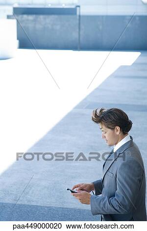 Businessman standing outdoors looking down at cell phone, high angle view View Large Photo Image Stock Image - Businessman standing outdoors looking down at cell phone, high angle view. Fotosearch