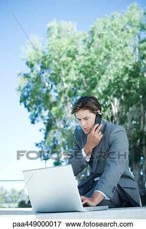 Businessman using laptop and cell phone, outdoors View Large Photo Image Stock Photo - Businessman using laptop and cell phone, outdoors. Fotosearch