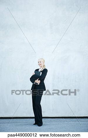 Stock Image - Businesswoman holding file against chest, laughing, full length portrait. Fotosearch