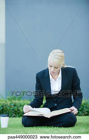 Businesswoman sitting on grass reading book, coffee cup nearby View Large Photo Image Stock Image - Businesswoman sitting on grass reading book, coffee cup nearby. Fotosearch