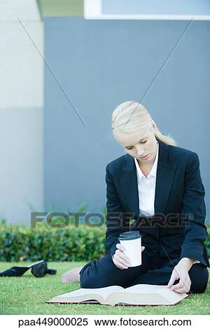Businesswoman sitting on grass reading book, holding coffee cup View Large Photo Image Stock Photography - Businesswoman sitting on grass reading book, holding coffee cup. Fotosearch