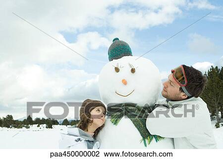 Stock Image - Brother and sister embracing snowman, smiling, head and shoulders. Fotosearch