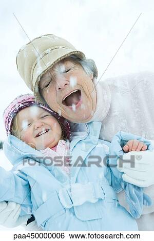 Stock Photograph - Senior woman and granddaughter cheek to cheek in snow, smiling, eyes, closed. Fotosearch