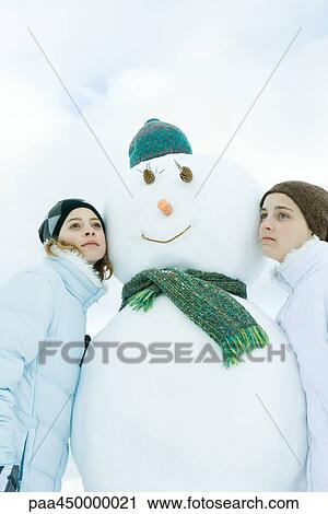 Two young friends leaning against snowman, looking away, portrait View Large Photo Image Stock Image - Two young friends leaning against snowman, looking away, portrait. Fotosearch
