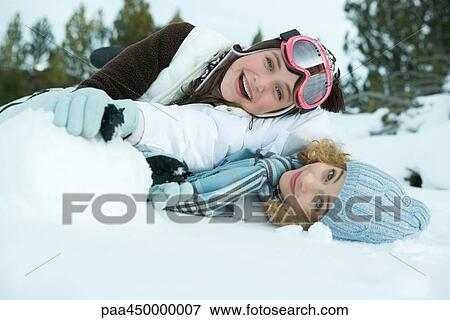 Two young friends reclining in snow, smiling at camera, one on top of the other View Large Photo Image Stock Photo - Two young friends reclining in snow, smiling at camera, one on top of the other. Fotosearch