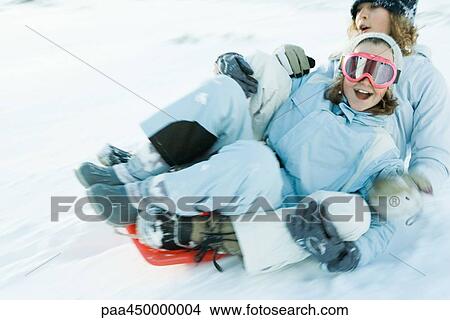 Picture - Two young friends riding sled together, blurred motion. Fotosearch