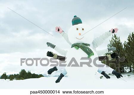 Picture - Young friends hiding behind snowman, arms outstretched. Fotosearch
