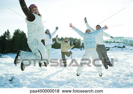 Stock Photo - Young friends jumping in the air, dressed in winter clothing, smiling at camera. Fotosearch