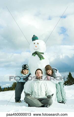 Young man meditating in front of snowman, two sisters crouching behind, smiling at camera View Large Photo Image Stock Image - Young man meditating in front of snowman, two sisters crouching behind, smiling at camera. Fotosearch