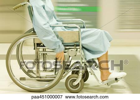 Stock Photo - Cropped view of man using wheelchair, dressed in hospital gown, blurred motion. Fotosearch