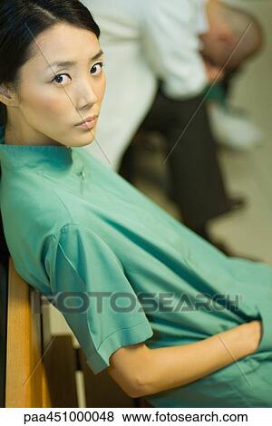 Female medical worker sitting with hand in pocket, looking at camera, doctor with head down in background View Large Photo Image Stock Photo - Female medical worker sitting with hand in pocket, looking at camera, doctor with head down in background. Fotosearch