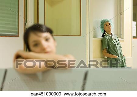 Stock Photo - Female surgeon standing with hands in pockets, looking at camera, woman resting head on arms in foreground. Fotosearch