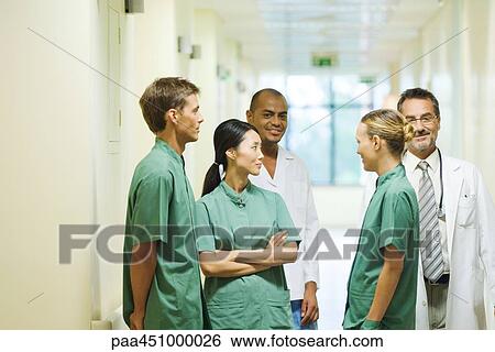 Group of medical staff standing in hallway, chatting, two looking at camera View Large Photo Image Stock Photograph - Group of medical staff standing in hallway, chatting, two looking at camera. Fotosearch