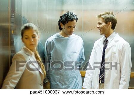 Male doctor chatting with patient in elevator, woman in foreground View Large Photo Image Stock Photo - Male doctor chatting with patient in elevator, woman in foreground. Fotosearch