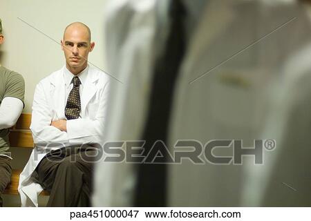 Male doctor sitting with arms folded, looking at camera, focus on background View Large Photo Image Stock Photo - Male doctor sitting with arms folded, looking at camera, focus on background. Fotosearch