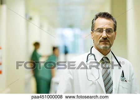 Stock Photo - Male doctor standing in hospital corridor, looking at camera, head and shoulders. Fotosearch