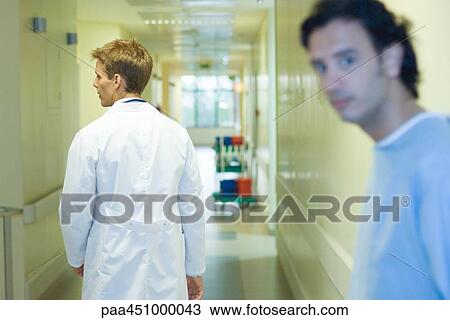 Male doctor walking in hospital corridor, rear view, man looking at camera in foreground View Large Photo Image Stock Image - Male doctor walking in hospital corridor, rear view, man looking at camera in foreground. Fotosearch