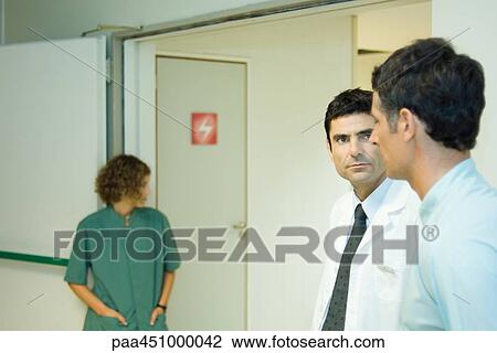 Man standing with doctor in hospital, side view, woman in background View Large Photo Image Stock Image - Man standing with doctor in hospital, side view, woman in background. Fotosearch