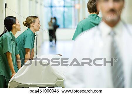 Medical staff pushing stretcher, looking away, doctor walking in foreground View Large Photo Image Stock Photography - Medical staff pushing stretcher, looking away, doctor walking in foreground. Fotosearch