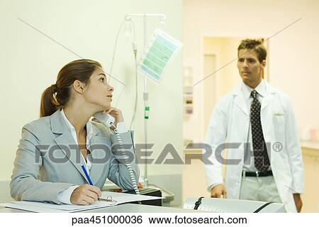 Woman using phone in doctor's office, looking over shoulder at male doctor View Large Photo Image Stock Photograph - Woman using phone in doctor's office, looking over shoulder at male doctor. Fotosearch