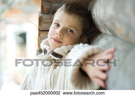 Stock Image - Boy standing next to log cabin, portrait. Fotosearch