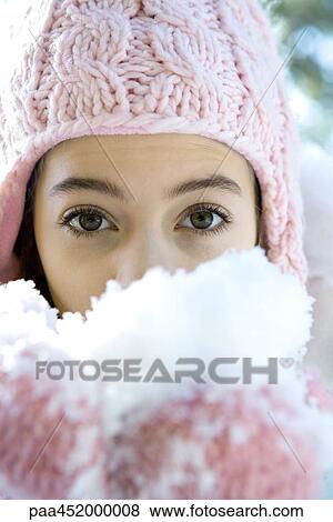 Stock Photo - Preteen girl holding handful of snow in mittens, looking at camera. Fotosearch
