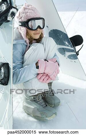 Stock Photography - Preteen girl sitting on snow underneath propped up snowboards. Fotosearch