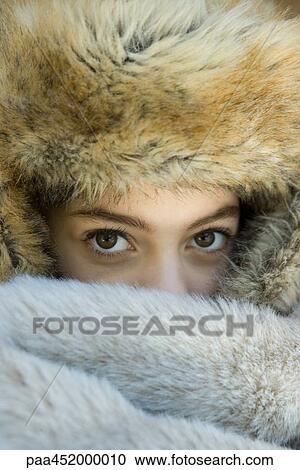 Stock Image - Preteen girl, wearing fur hat, looking over fur blanket, close-up. Fotosearch
